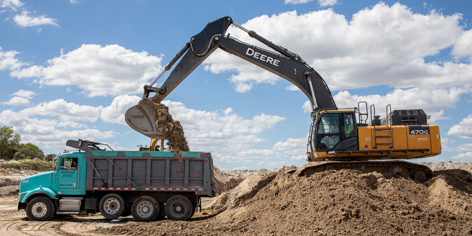 excavator dumping fill dirt into construction truck