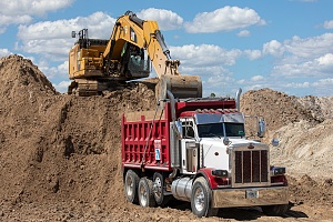 excavator filling up the back of a truck with fill dirt