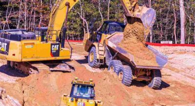 power shovel fills a dump truck with dirt to clear land for home construction
