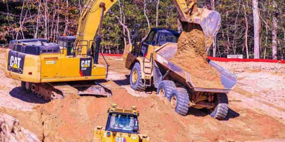 power shovel fills a dump truck with dirt to clear land for home construction